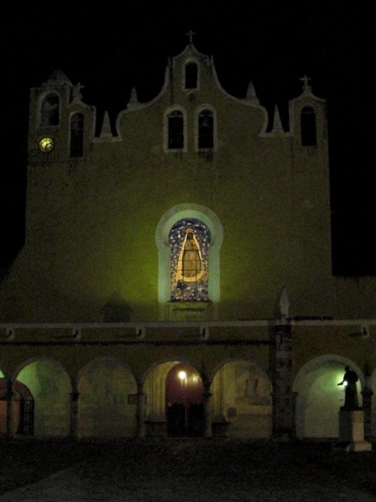 P’ap’hol Chaak - Front der Klosterkirche mit Glasfenster bei Nacht - die Figur vorne rechts stellt Diego di Landa dar