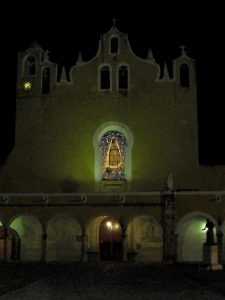 P’ap’hol Chaak - Front der Klosterkirche mit Glasfenster bei Nacht - die Figur vorne rechts stellt Diego di Landa dar